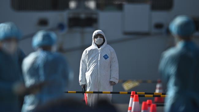 Workers in protective clothes stand before passengers disembarkating off the Diamond Princess cruise ship. Picture: AFP