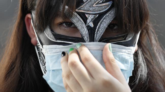 Lucha Libre wrestler Hija de la Zorra adjusts a surgical mask atop her wrestling mask as she waits in line to receive a donation of household items, in Mexico City. Picture: Rebecca Blackwel/AP