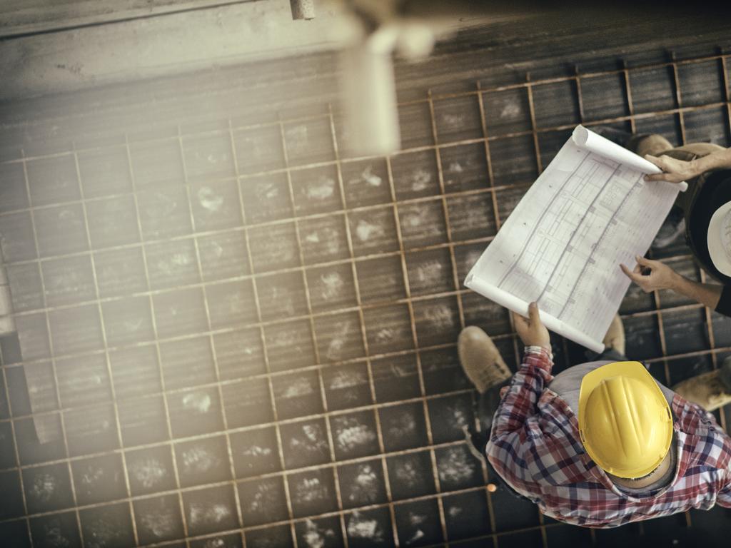 High angle view of three people with helmets, female architect, foreman and engineer on a construction site, looking down on a blueprint, copy space.