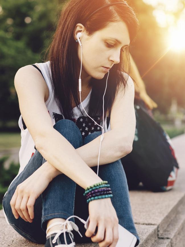 Depressed woman sitting outside and listening to the music from smartphone