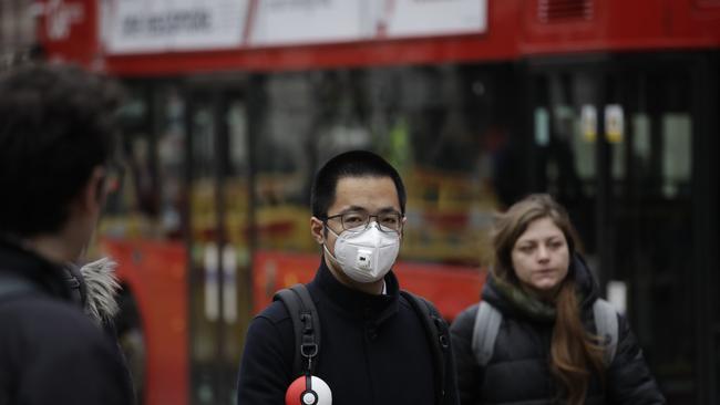 A man wearing a face mask walks backdropped by a red London bus across the street from the Bank of England in London. Picture: AP