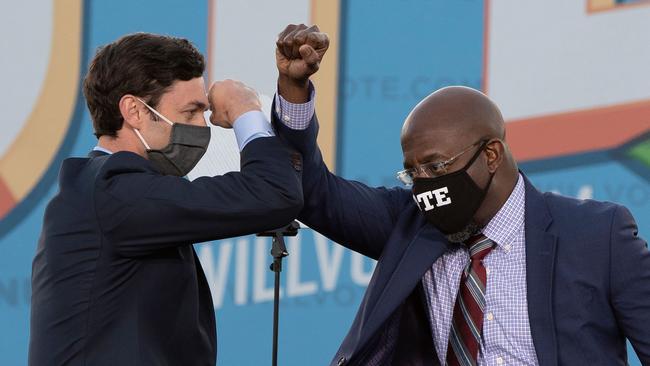 Jon Ossoff (L) and Raphael Warnock (R) bump elbows on stage during a rally with US President-elect Joe Biden outside Center Parc Stadium in Atlanta, Georgia.