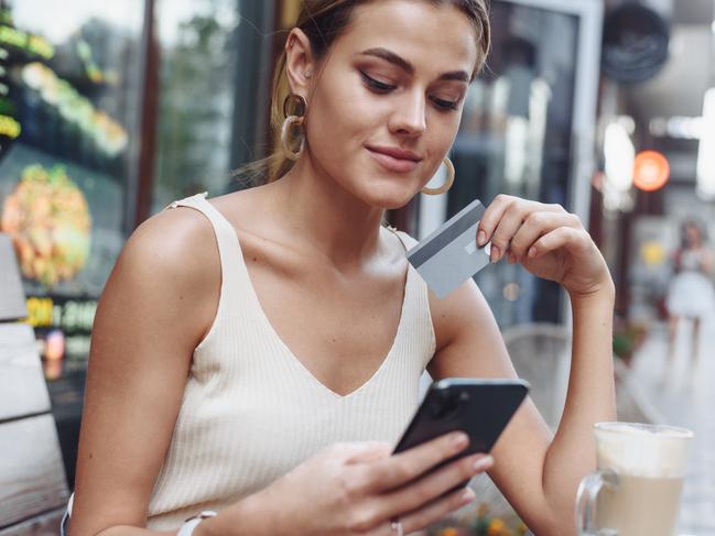 Woman sitting at cafe holding mobile phone and plastic card signing up on website.Beautiful model paying with credit card while shopping online using mobile.