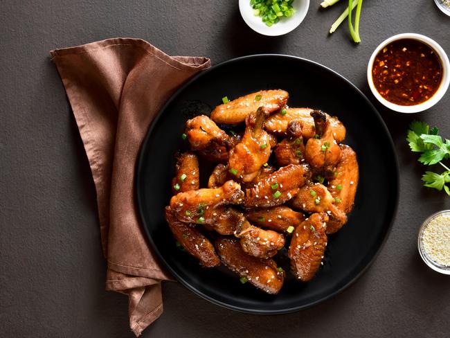 Sticky honey-soy chicken wings on plate over dark stone background. Top view, flat lay, close up