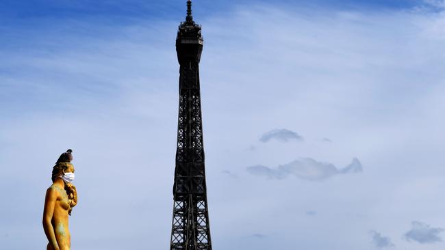 The Eiffel Tower is seen as a backdrop to bronze statues, one dressed in a mask across her nose and mouth, emulating the actions of many citizens to protecting themselves against the novel coronavirus. Picture: AFP