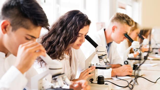 Beautiful high school students with microscopes in laboratory during biology class.