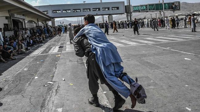 A volunteer carries an injured man as other people can be seen waiting at Kabul airport on Monday. Picture: AFP