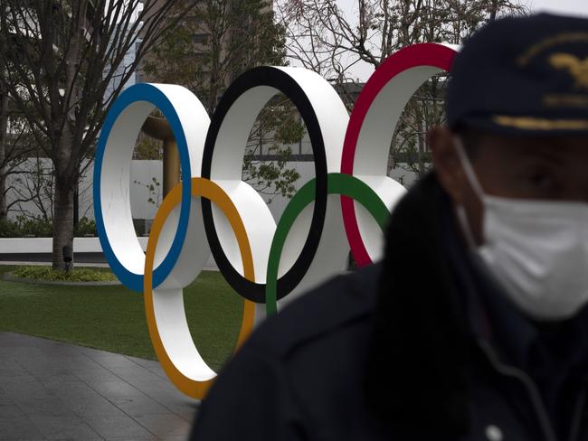 A security guard walks past the Olympic rings near the New National Stadium in Tokyo, Monday, March 23, 2020. The IOC will take up to four weeks to consider postponing the Tokyo Olympics amid mounting criticism of its handling of the coronavirus crisis that now includes a call for delay from the leader of track and field, the biggest sport at the games. (AP Photo/Jae C. Hong)