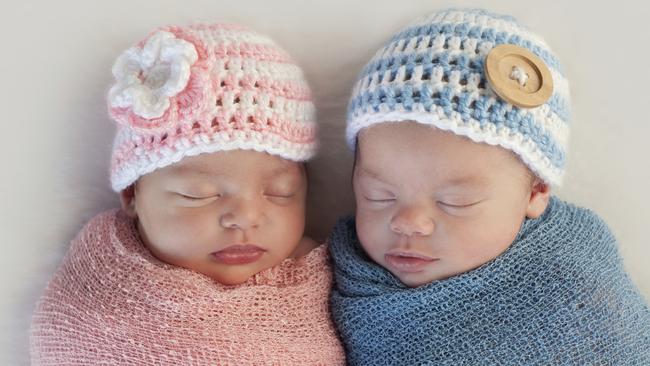 Five week old sleeping boy and girl fraternal twin newborn babies. They are wearing crocheted pink and blue striped hats.