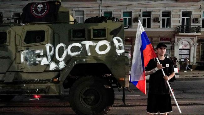 A man holds the Russian national flag in front of a Wagner group military vehicle.