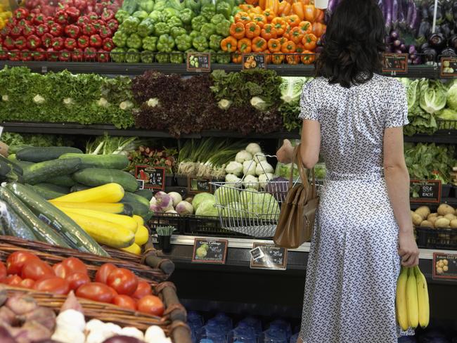 Fruit prices. Rear view of a woman holding a basket and bananas in the produce aisle of a supermarket. Shopping. Generic image.