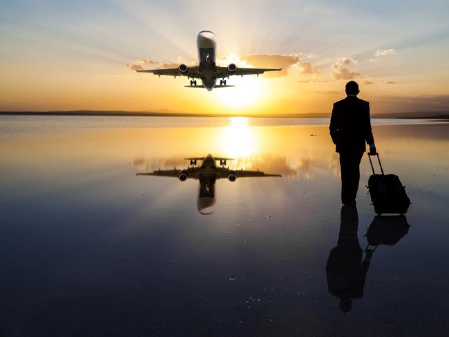 Businessman pulling his luggage and walking against sun while a passenger plane passes over. **PIC IDEA FOR 'NOWHERE' TRAVEL STORY**