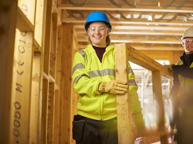 a female construction worker carries some studwork on a building site housing development and is assited by a male colleague .