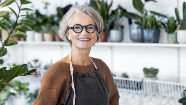 Portrait of senior female florist at small business flower shop. Happy mature woman wearing apron working in a small flower store; working in retirement happy retiree worker generic