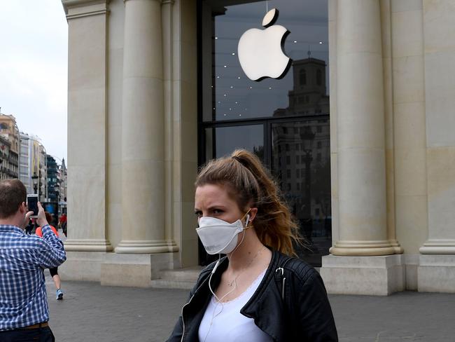 A woman wearing a face mask walks past the closed Apple store in Barcelona on March 14, 2020 after regional authorities ordered all shops in the region be shuttered from today through March 26, save for those selling food, chemists and petrol stations, in order to slow the coronavirus spread. (Photo by Josep LAGO / AFP)