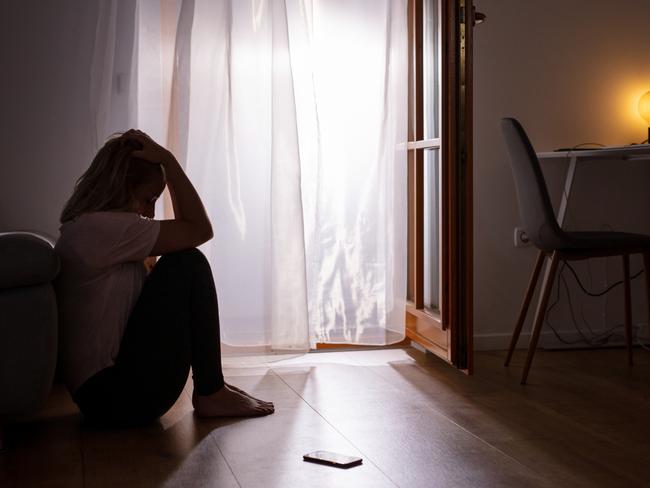 Side view full length shot of a sad depressed woman sitting on the floor and crying at home