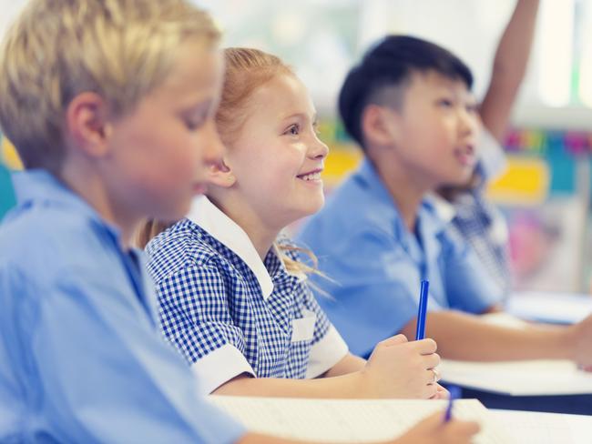 Group of children listening to the teacher. They are in a classroom. Multiethnic group with Caucasian and Asian kids. School girl is smiling and happy