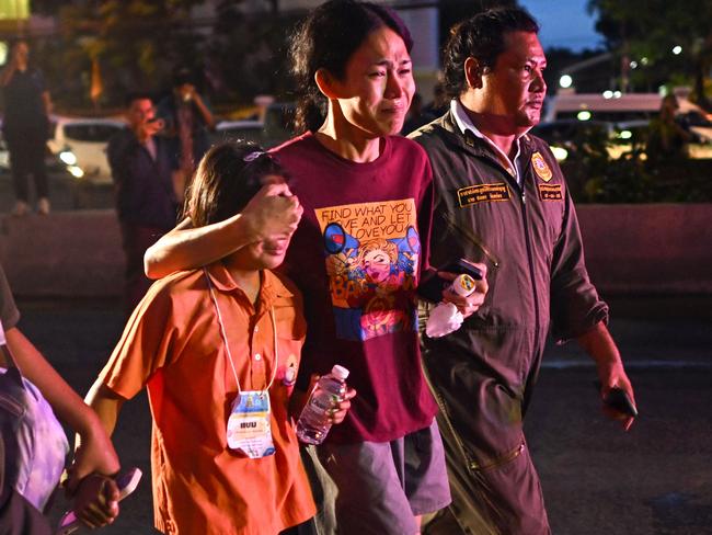 A relative of a student who died in a bus fire covers the eyes of a child travelling on a separate bus on the same school trip so they don’t have to see the wreckage. Picture: AFP.