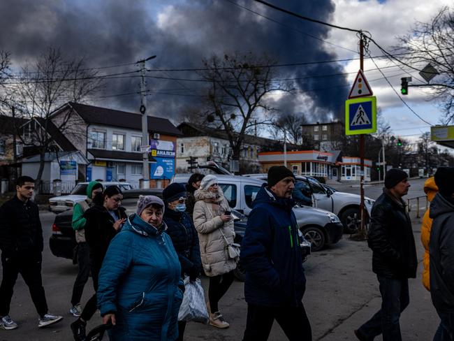 People stand in line in front of a supermarket while smoke billows over the town of Vasylkiv just outside Kyiv. Picture: AFP