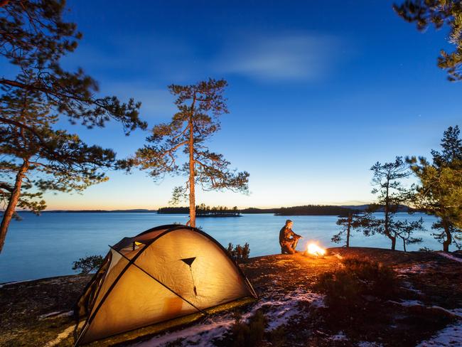 ESCAPE: Camping Etiquette, . Man is sitting around a campfire and just relaxing, snow on the ground . Picture: iStock