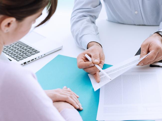 CAREERS: Young woman meeting a professional consultant in his office, he is holding a document and giving explanations.