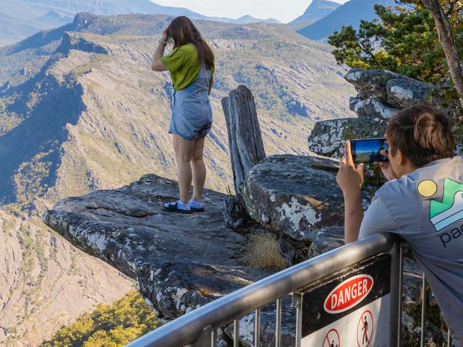 A woman standing on “selfie rock” for a photo, despite a warning sign. Picture: Jason Edwards