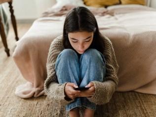 Teenage girl sitting on the floor and scrolling a smartphone.