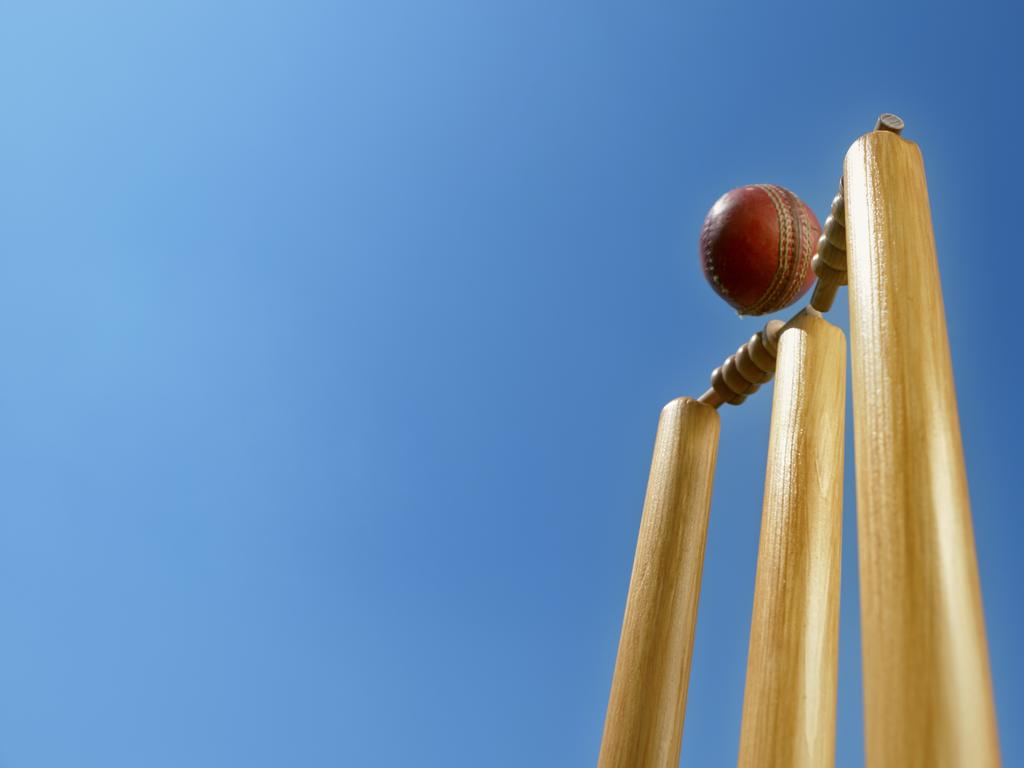 Close-up of cricket ball hitting the stumps and knocking off the bails against sky.