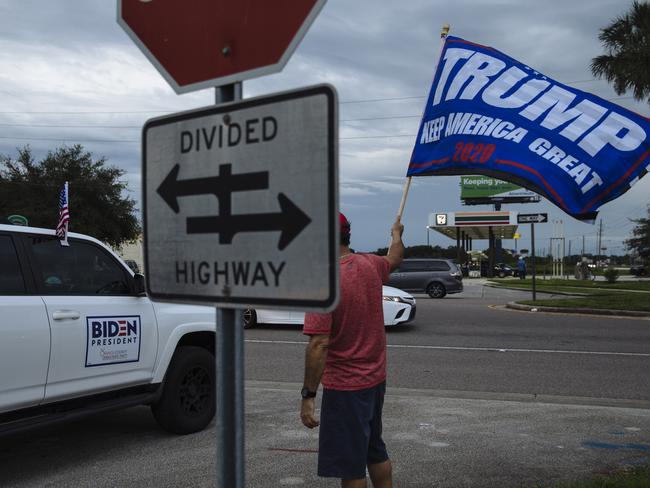 A Trump supporter waves a flag next to a car with Pro-Biden stickers. Picture: Angus Mordant for NewsCorp Australia