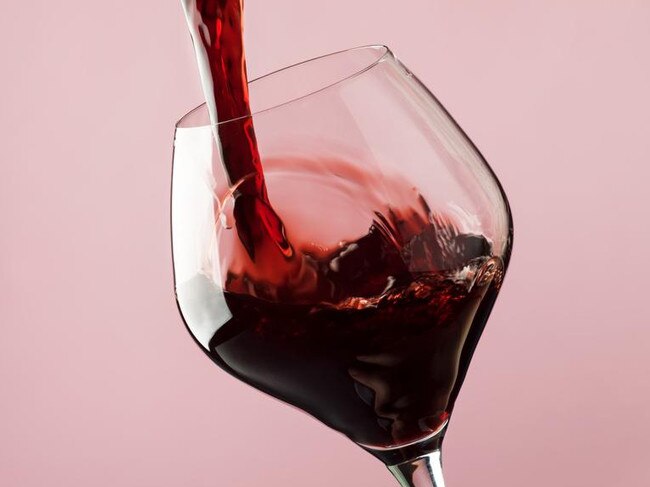 French dry red wine, pours into glass, trendy pink background, space for text, selective focus