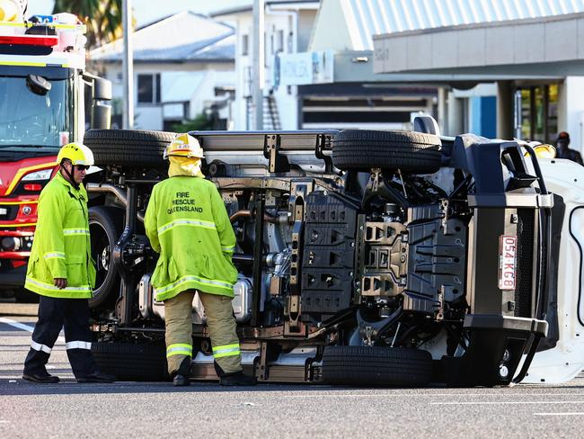Queensland Fire and Emergency Services firefighters attend to the scene of a traffic collision between two utilities at the intersection of Sheridan and Minnie Streets, where one ute rolled onto its side. Picture: Brendan Radke