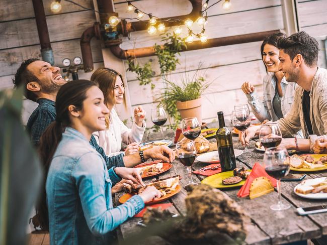 Young people dining and having fun drinking red wine together on balcony rooftop dinner party - Happy friends eating bbq food at restaurant patio - Millannial life style concept on warm evening filter