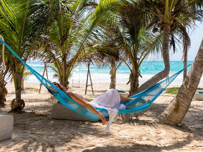 Woman relaxing in a hammock on a tropical beach with palm trees and turquoise waters