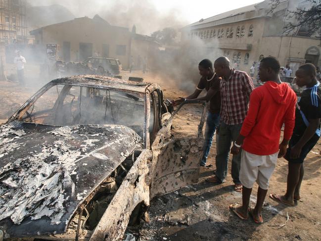 Men look at the burnt-out wreckage of a car following a bomb blast at St Theresa Catholic Church outside the Nigerian capital Abuja, 25/12/2011. Two explosions near churches during Christmas Day services in Nigeria, including one outside the country's capital, killed at least 28 amid spiralling violence blamed on an Islamist group and the suspected attacks stoked fear and anger in Africa's most populous nation, which has been hit by scores of bombings and shootings attributed to Islamist group Boko Haram, with authorities seemingly unable to stop them.