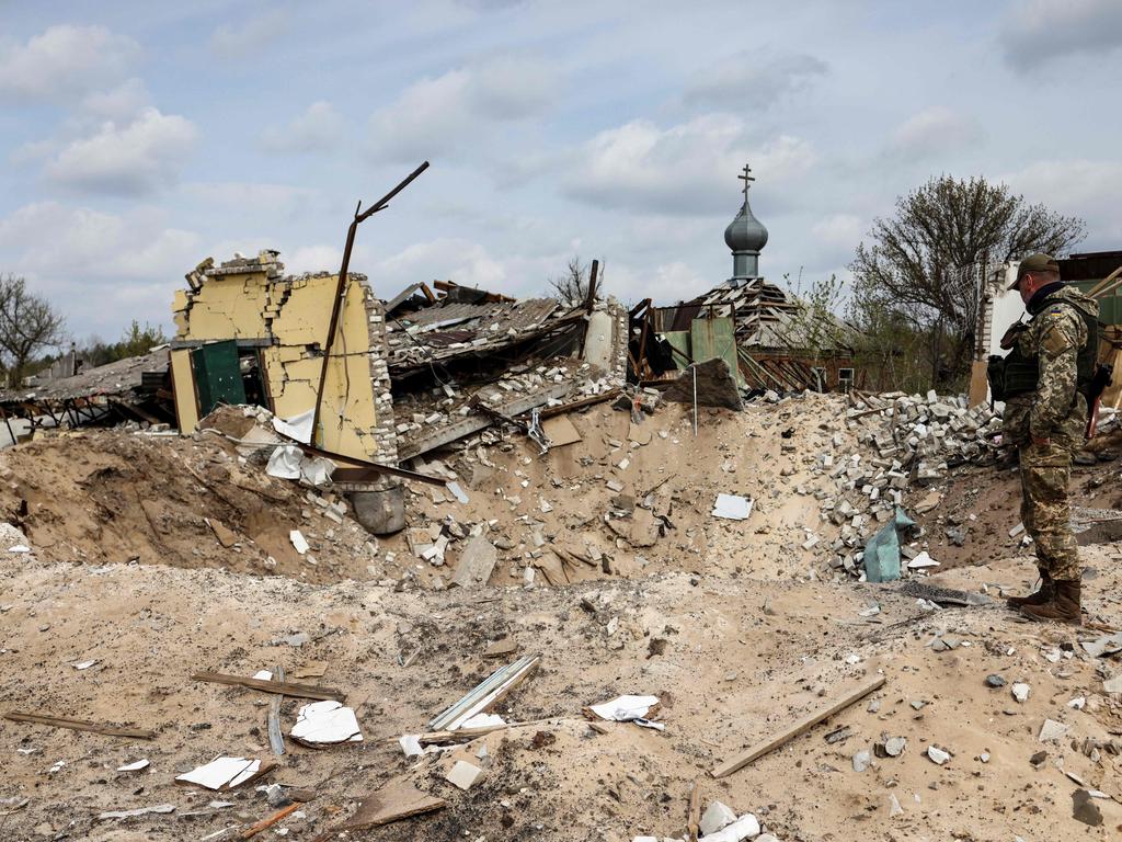 A Ukrainian serviceman looks into a crater and a destroyed home are pictured in the village of Yatskivka, eastern Ukraine. The bombings by Russia continue according to officials. Picture: AFP