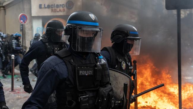 PARIS, FRANCE - MARCH 28: Police officers pass by a fire as they charge protesters during a rally against pension reforms on March 28, 2023 in Paris, France. The country has experienced weeks of protests and strike actions related to a rise in the pension age, which was passed last week. The 10th day of nationwide protests in France against the pension reforms are also calling out the police brutality from pervious strikes. (Photo by Carl Court/Getty Images)