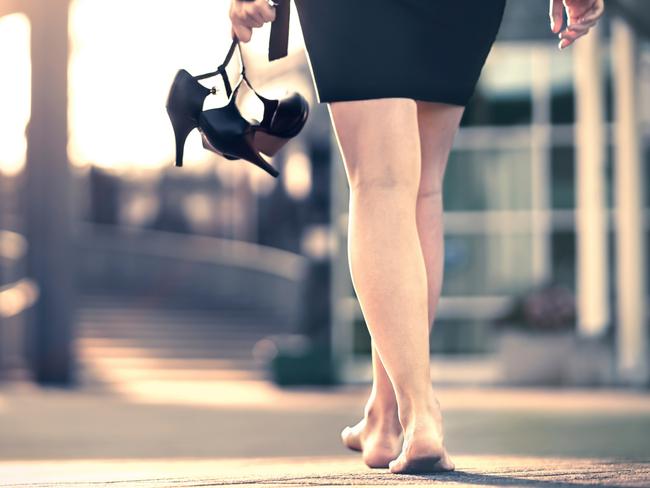 Woman holding high heels in hand and walking home from party barefoot. Businesswoman took off uncomfortable shoes. Lady with stilettos and miniskirt at sunrise or sunset in city street. Walk of shame.