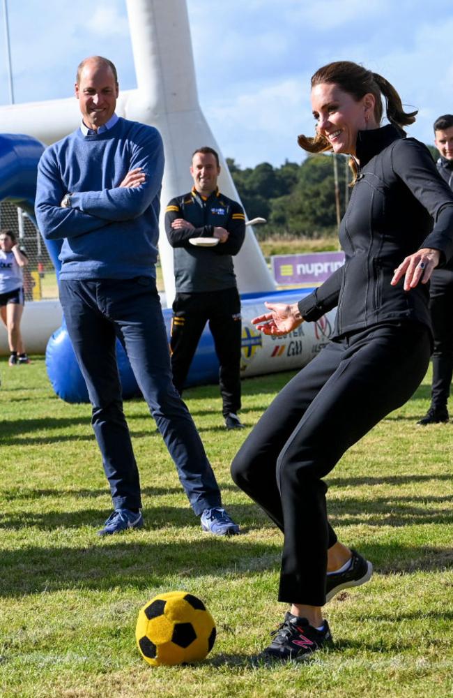 LONDONDERRY, NORTHERN IRELAND - SEPTEMBER 29: Catherine, Duchess of Cambridge kicks a football as Prince William, Duke of Cambridge looks on during a visit to the City of Derry Rugby Club on September 29, 2021 in Londonderry, Northern Ireland. The Duke and Duchess of Cambridge arrive in Derry-Londonderry where they will spend the day meeting young people and hearing how organisations are engaging across communities to promote positive relations. It is Their Royal Highnesses' first time in this area of Northern Ireland. (Photo by Tim Rooke - Pool /Getty Images)