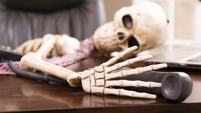 Skeleton of a man who has died while waiting "on hold" on his office telephone.  He wears necktie and has laptop on desk.