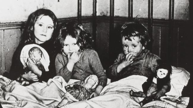 Three children huddle in a single bedroom in a slum house in Erskine Place, North Melbourne. Picture: F. Oswald Barnett collection, State Library of Victoria