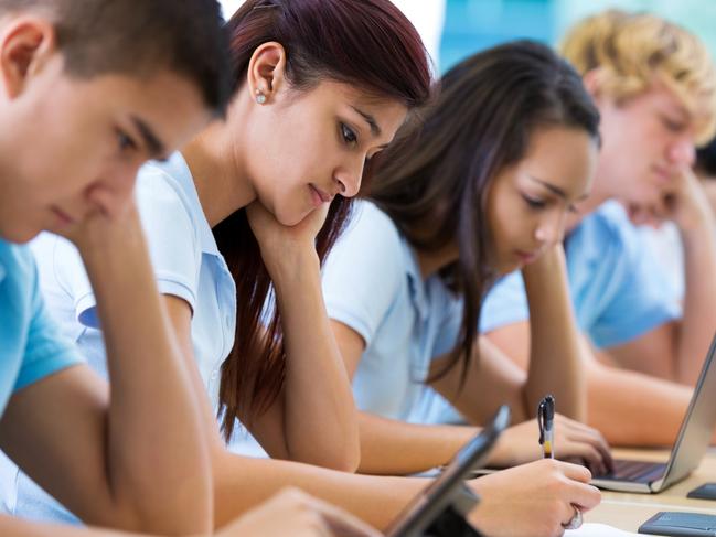 Row of private high school students work on assignment in class. They are writing or using laptops or digital tablets. They are concentrating as they study. They are wearing school uniforms. Picture: iStock