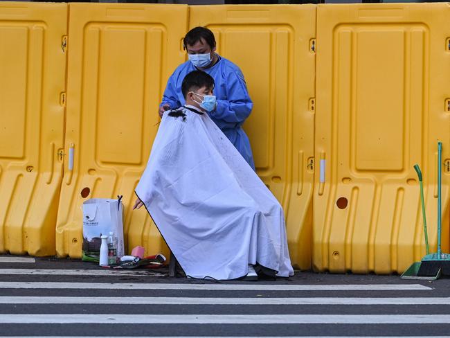 A man has a haircut on a street next to a locked down neighbourhood during a coronavirus lockdown in the Jing'an district of Shanghai. Picture: AF)