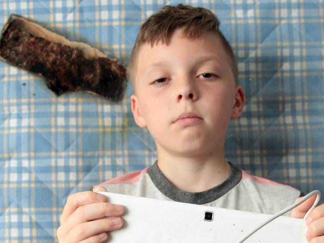 ONE TIME WEB USE ONLY - FEE APPLIES FOR REUSE -  Pic By  Dilantha Dissanayake / Mercury Press and Media  (PICTURED: Callum Hewkin holding burnt Samsung tablet in front of burnt mattress Pic Taken 23/06/2019)  - The parents of an 11-year-old boy who could have died when his Samsung tablet burnt a gaping hole inches from his head have spoken out about the terrifying ordeal. Dad-of-one Stewart Hewkin, 32, and wife Amy Williams, 34, were horrified after waking last Thursday [JUNE 20] to find 11-year-old son Callum asleep next to a giant hole burned through his bed where the gadget had been charging. - SEE MERCURY COPY  Picture: Mercury Press/Caters News