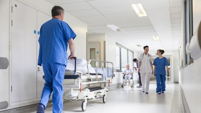 Male nurse pushing stretcher gurney bed in hospital corridor with doctors & senior female patient