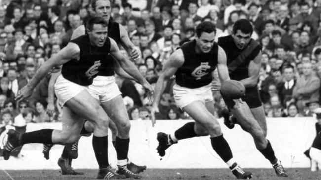 John Nicholls and Wes Lofts look on as Geoff Gosper chases Ron Barassi.