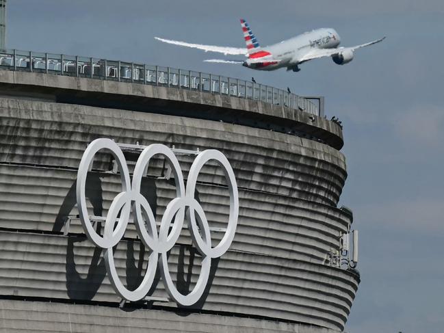 This photograph taken in Roissy-en-France on April 23, 2024, shows the Olympic rings on the Roissy - Charles de Gaulle Airport terminal 1, as an aircraft takes off. The Paris 2024 Olympics will take place from July 26 to August 11, 2024. (Photo by Miguel MEDINA / AFP)