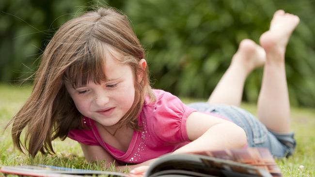 little girl laying in grass reading. Childrens Week. Thinkstock Image