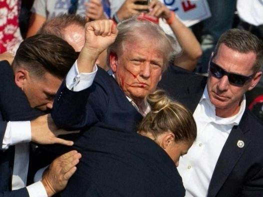 TOPSHOT - Republican candidate Donald Trump is seen with blood on his face surrounded by secret service agents as he is taken off the stage at a campaign event at Butler Farm Show Inc. in Butler, Pennsylvania, July 13, 2024. Republican candidate Donald Trump was evacuated from the stage at today's rally after what sounded like shots rang out at the event in Pennsylvania, according to AFP. The former US president was seen with blood on his right ear as he was surrounded by security agents, who hustled him off the stage as he pumped his first to the crowd. Trump was bundled into an SUV and driven away. (Photo by Rebecca DROKE / AFP)