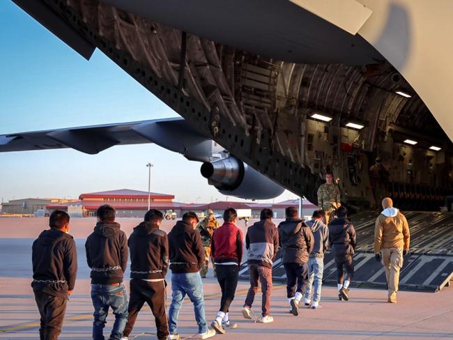 Nine restrained young men are led to a military plane as the military watch on. Picture: posted on X by White House press secretary Karoline Leavitt