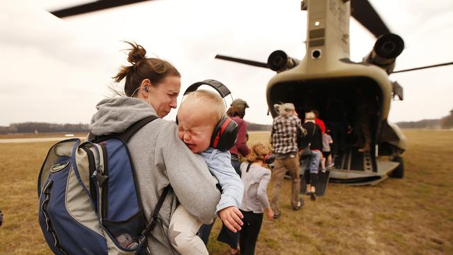 A baby in mum's arms cries as they approach the noise and heat from the turbine engines of the running Chinook helicopter bound for Sale, from Mallacoota. Picture: David Caird